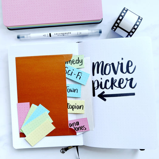 Open a5 journal with title movie picker and envelope of pastel paper with genres and film names