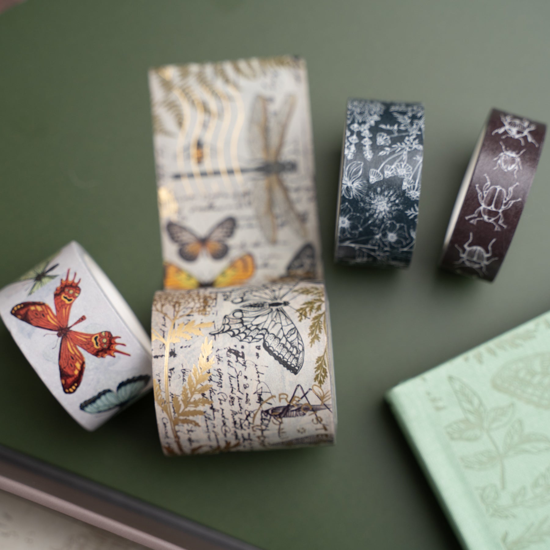 Decorative washi tape rolls with nature-themed designs on a green surface.