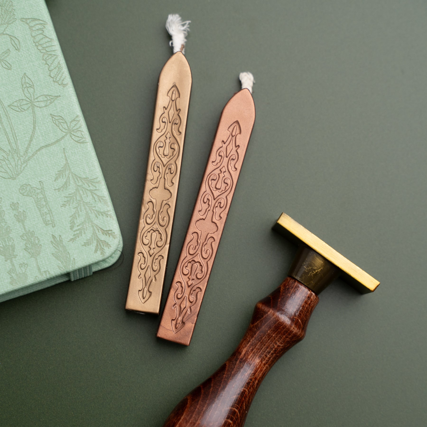 Two leather wax sticks with intricate designs on a green surface, accompanied by a wooden tool.
