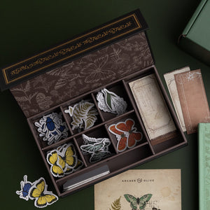 Set of butterfly-themed patches in a decorative box on a dark surface.