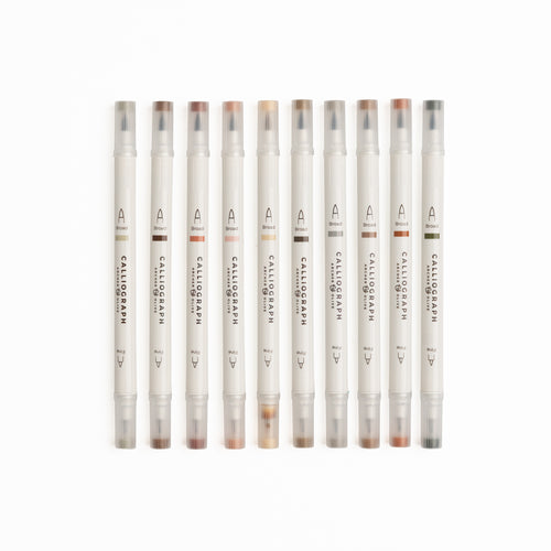 Set of ten Quiet Corners calligraphy pens with flexible brush tips laid out with lettering samples