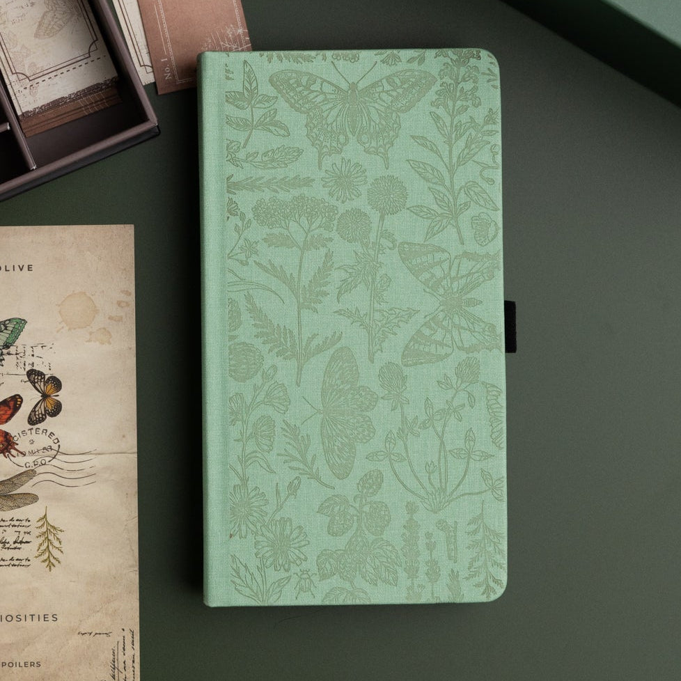 Green notebook with butterfly and floral pattern on a dark surface