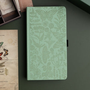 Green notebook with butterfly and floral pattern on a dark surface