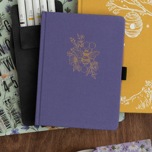 Purple notebook with floral and bee design on a wooden surface