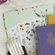 Notebooks and stationery items with floral designs on a light background