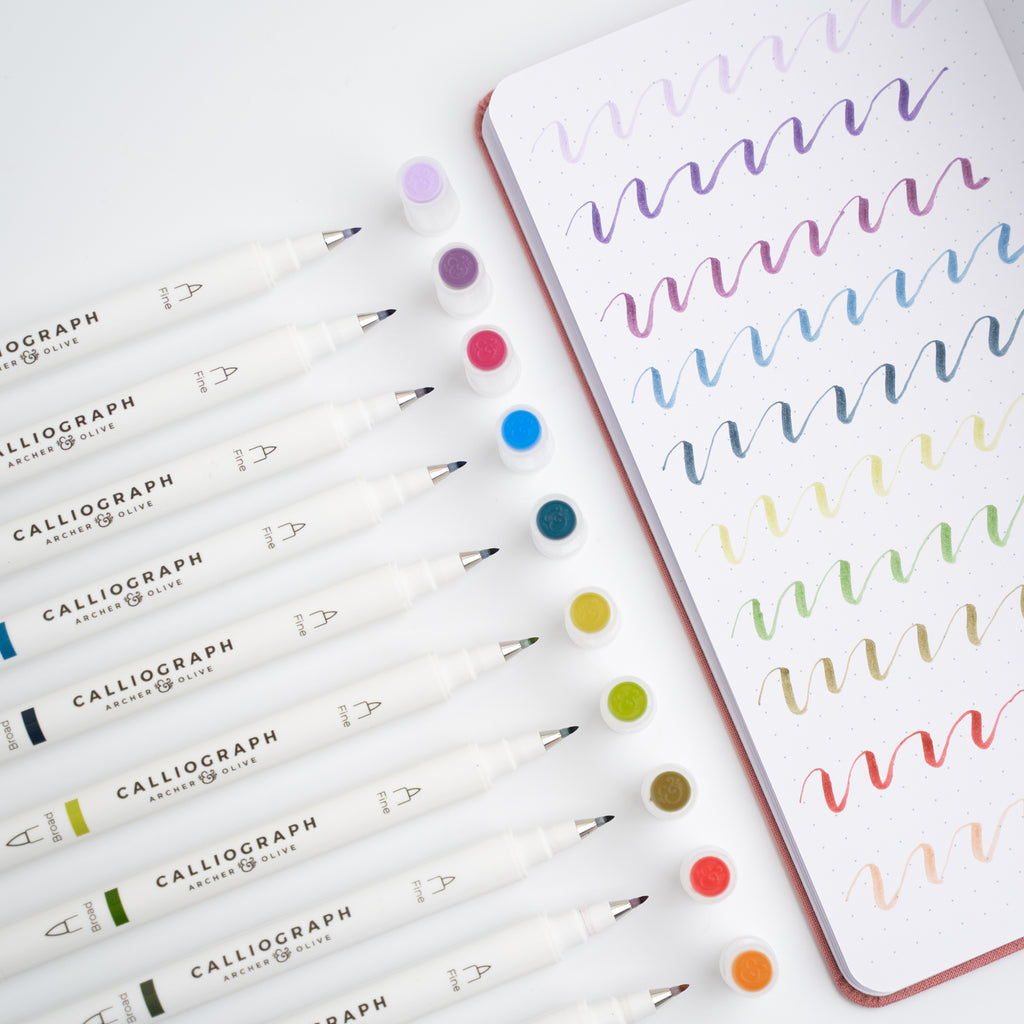Set of Calliograph markers with a notebook featuring colorful calligraphy on a white background