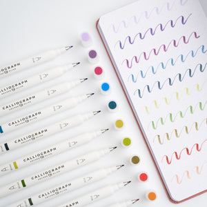 Set of Calliograph markers with a notebook featuring colorful calligraphy on a white background