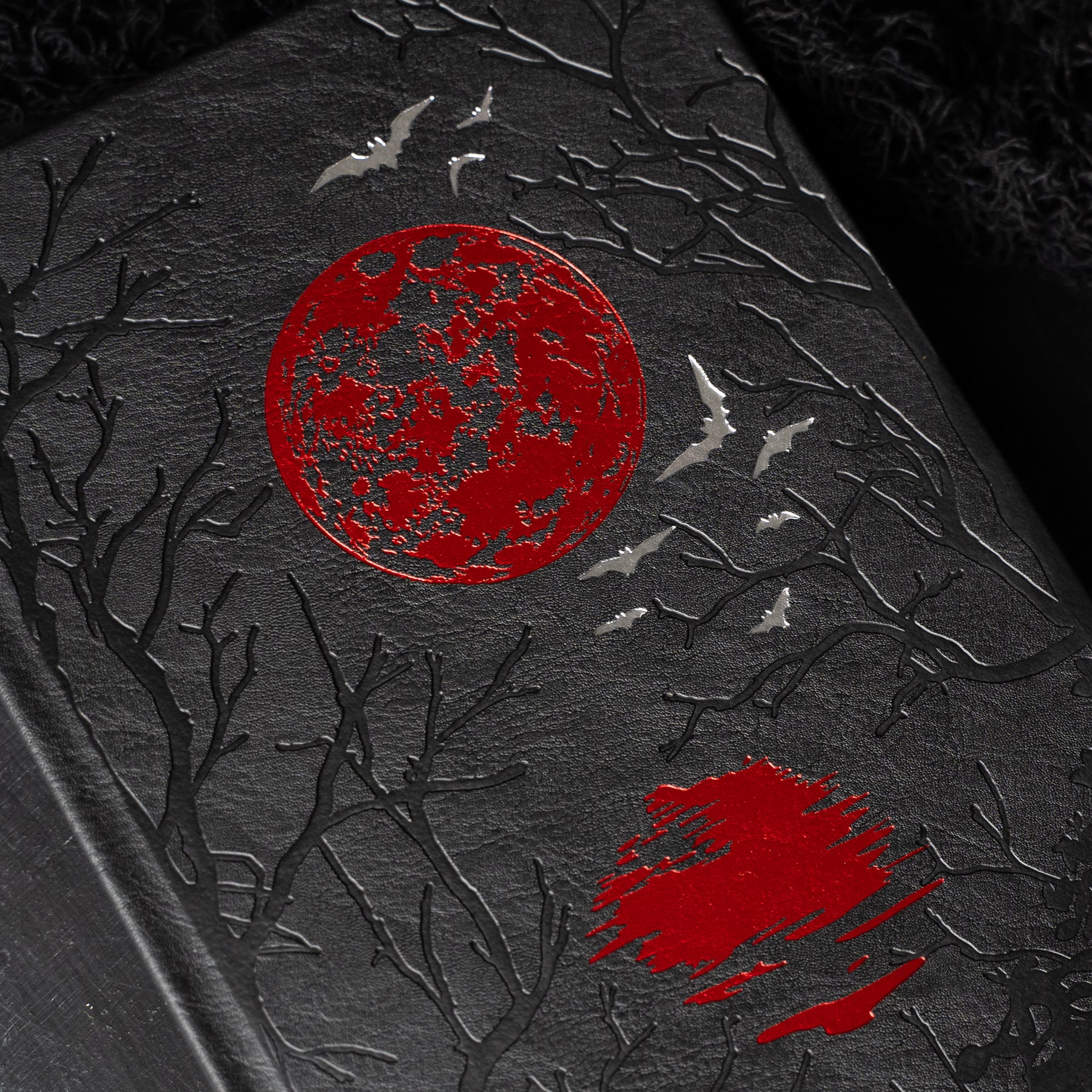 Dark leather-bound book with red moon and bats design on a dark background