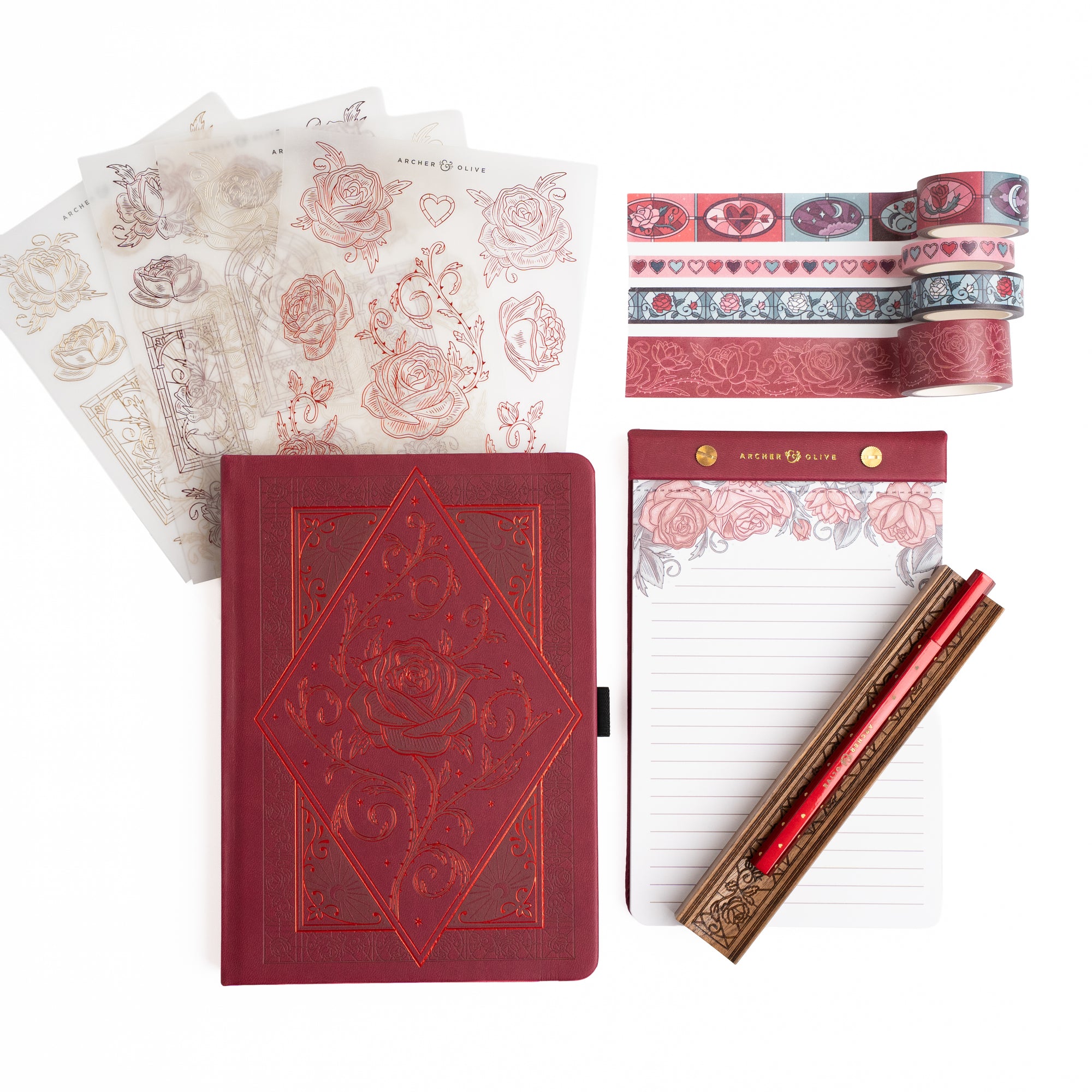 Stationery items including a red notebook, decorative paper, tape, and pen on a white background